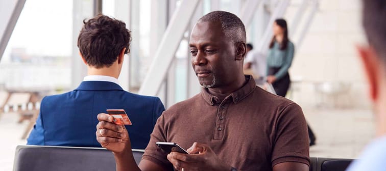 Businessman Sitting In Airport Departure Lounge Shopping Online Using Mobile Phone