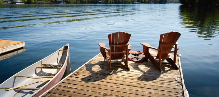 Two Adirondack chairs on a wooden dock facing the blue water