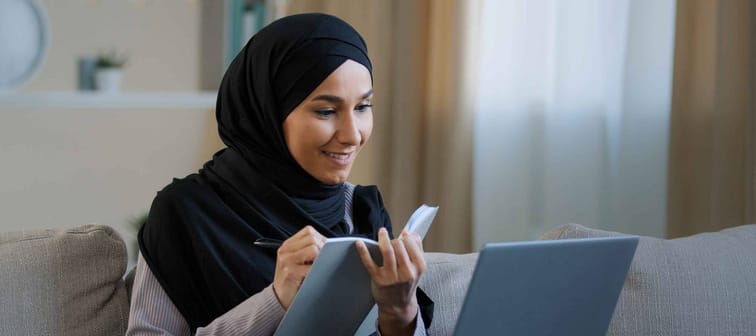Cheerful young muslim arabian lady young woman on couch with laptop