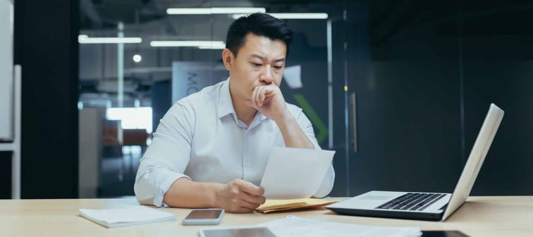 Stressed young asian businessman working from office report annoyed with low sales. Nervous boss see c mistake incorrect information in paper document