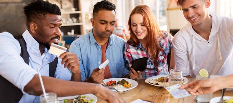 leisure, payment and people concept - happy friends with money and credit card paying bill for food at restaurant