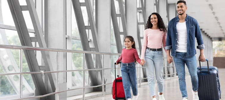 Travel Advertisement. Portrait Of Happy Arab Family Walking With Luggage At Airport, Beautiful Middle Eastern Mother, Father And Little Daughter Going To Boarding, Enjoying Traveling Together