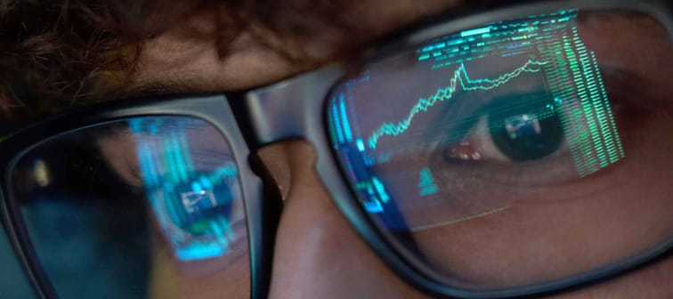 Young indian business man trader wearing glasses looking at computer screen with trading charts reflecting in eyeglasses watching stock trading market financial data growth concept, close up.