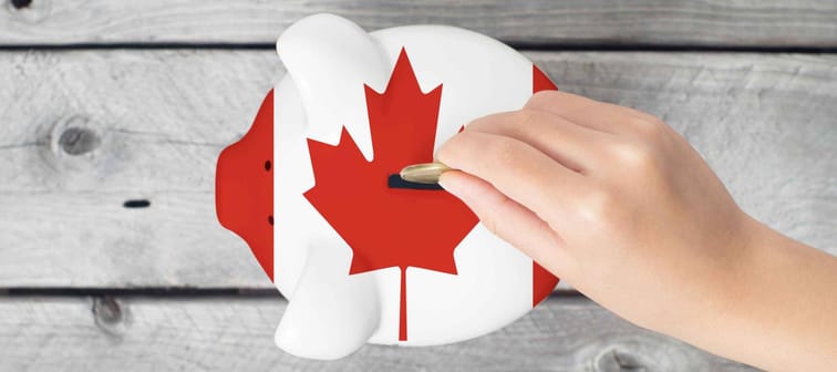 Canada saving concept with little hand dropping a coin into piggy bank overlaid with Canadian flag
