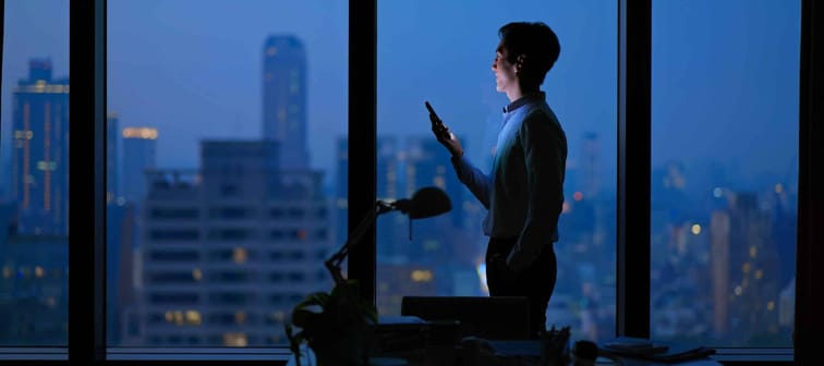 Side view of Asian business man standing in office using smartphone at night