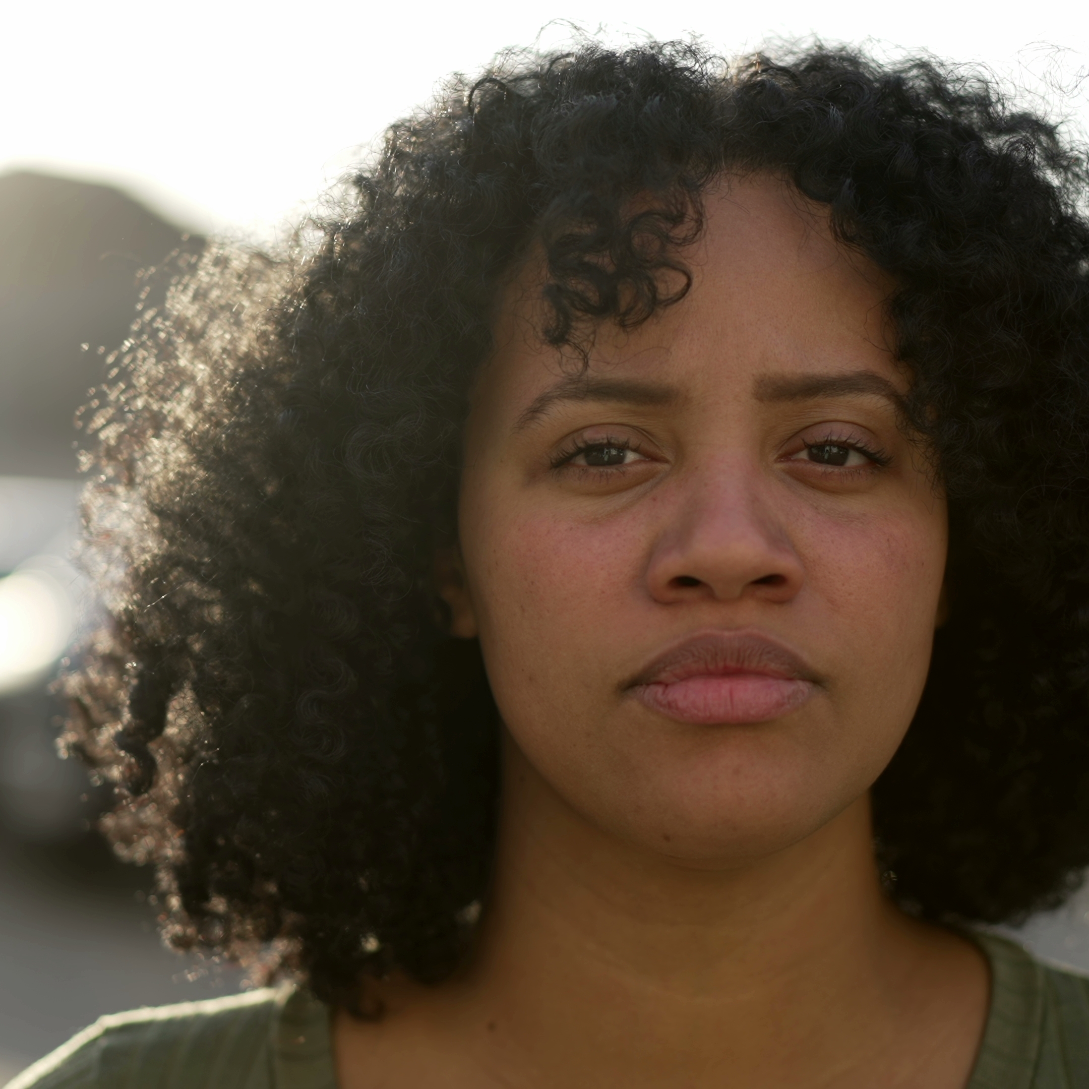One young black woman standing outdoors with serious expression.