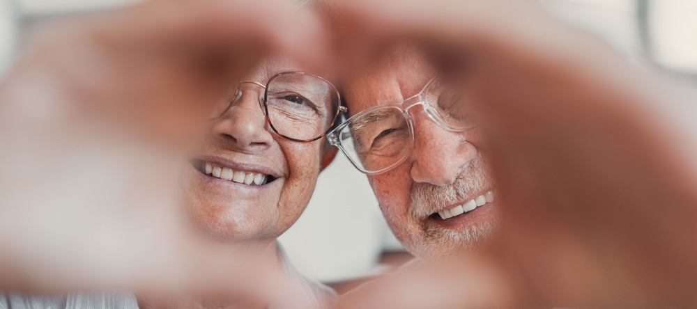 Happy senior couple smiling and holding hands together in a heart shape