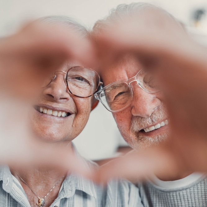 Happy senior couple smiling and holding hands together in a heart shape