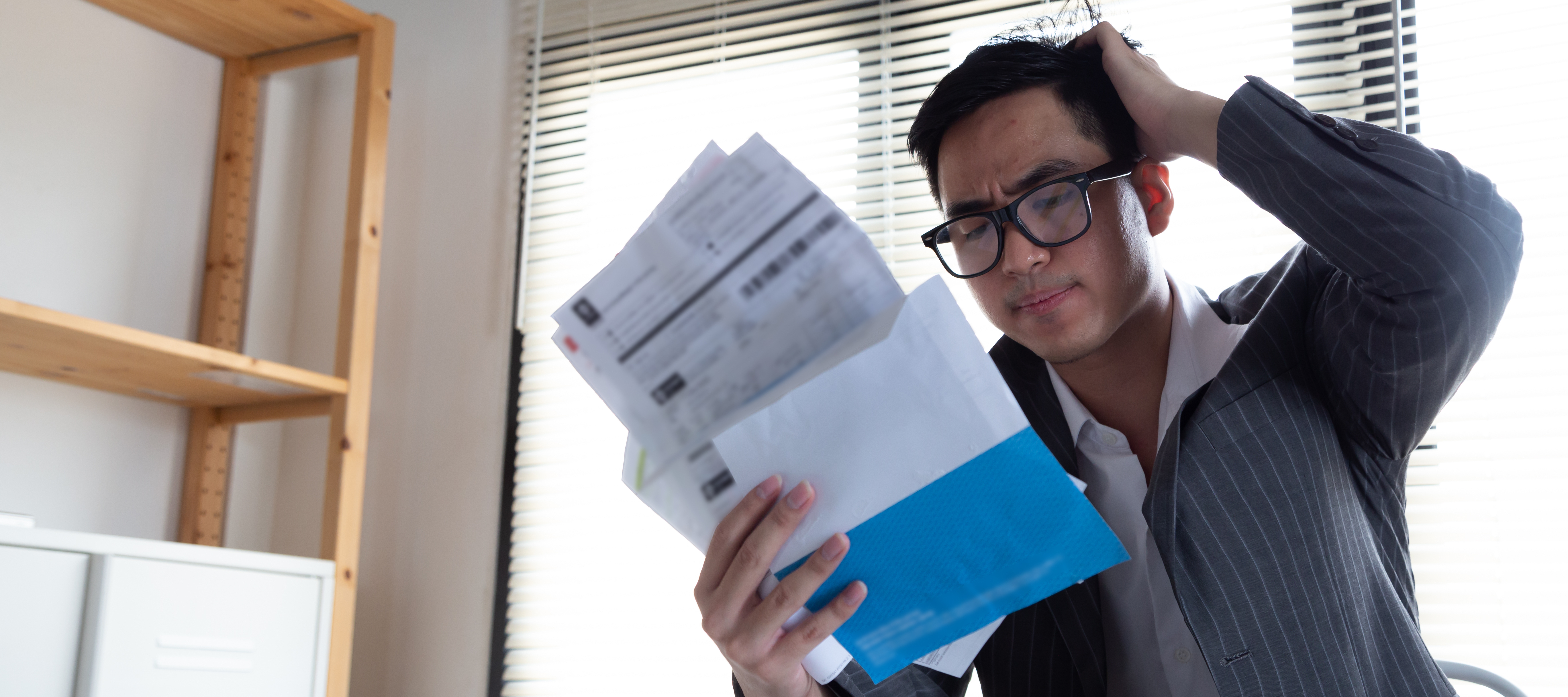 Sad confused and stressed young Asian man holding bills and credit card statements.