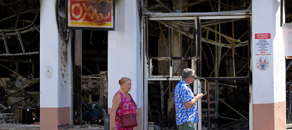 Tourists walk past a burned shop in Puerto Vallarta, Jalisco State, Mexico, on February 24, 2026