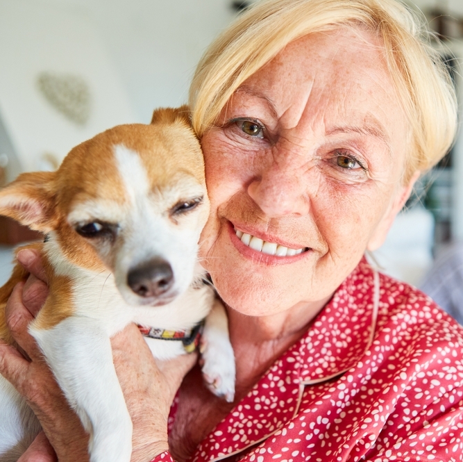 Happy elderly woman with a small dog in her arms at home