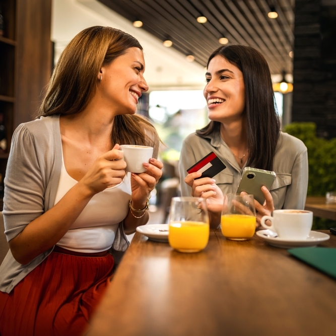 Two female friends enjoy a coffee out while paying by credit card