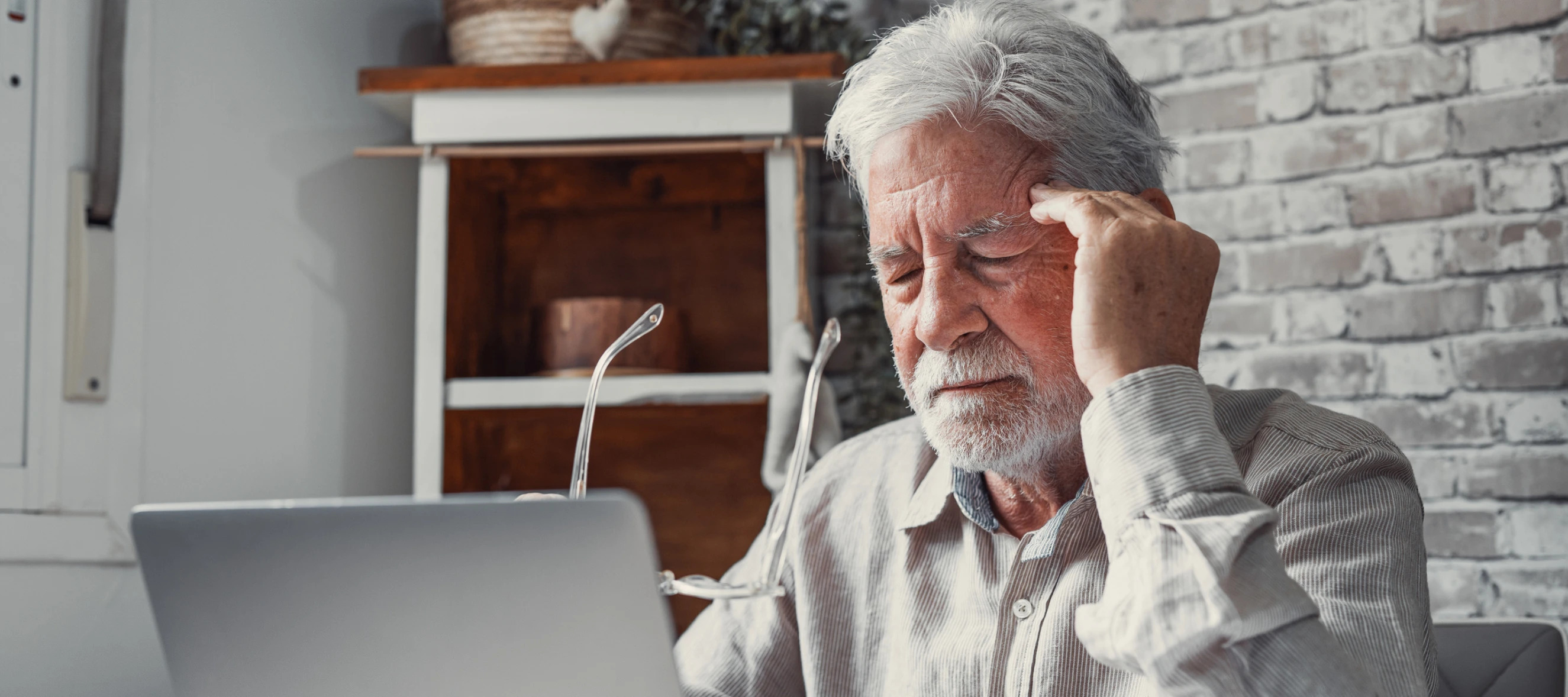 Man on laptop holding glasses in his hands and pushing on his temples like he has a headache