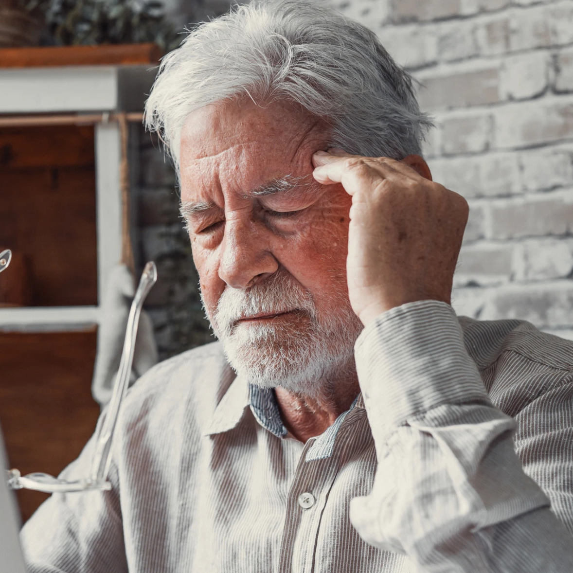 Man on laptop holding glasses in his hands and pushing on his temples like he has a headache