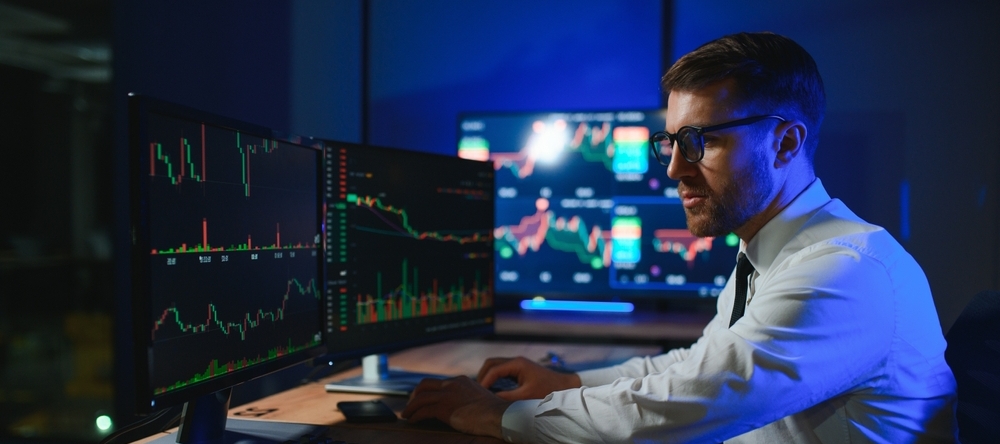 Young male professional stock trader at desk with computers showcasing stock tickers