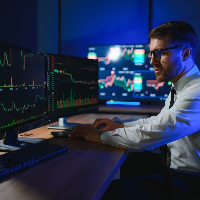Young male professional stock trader at desk with computers showcasing stock tickers
