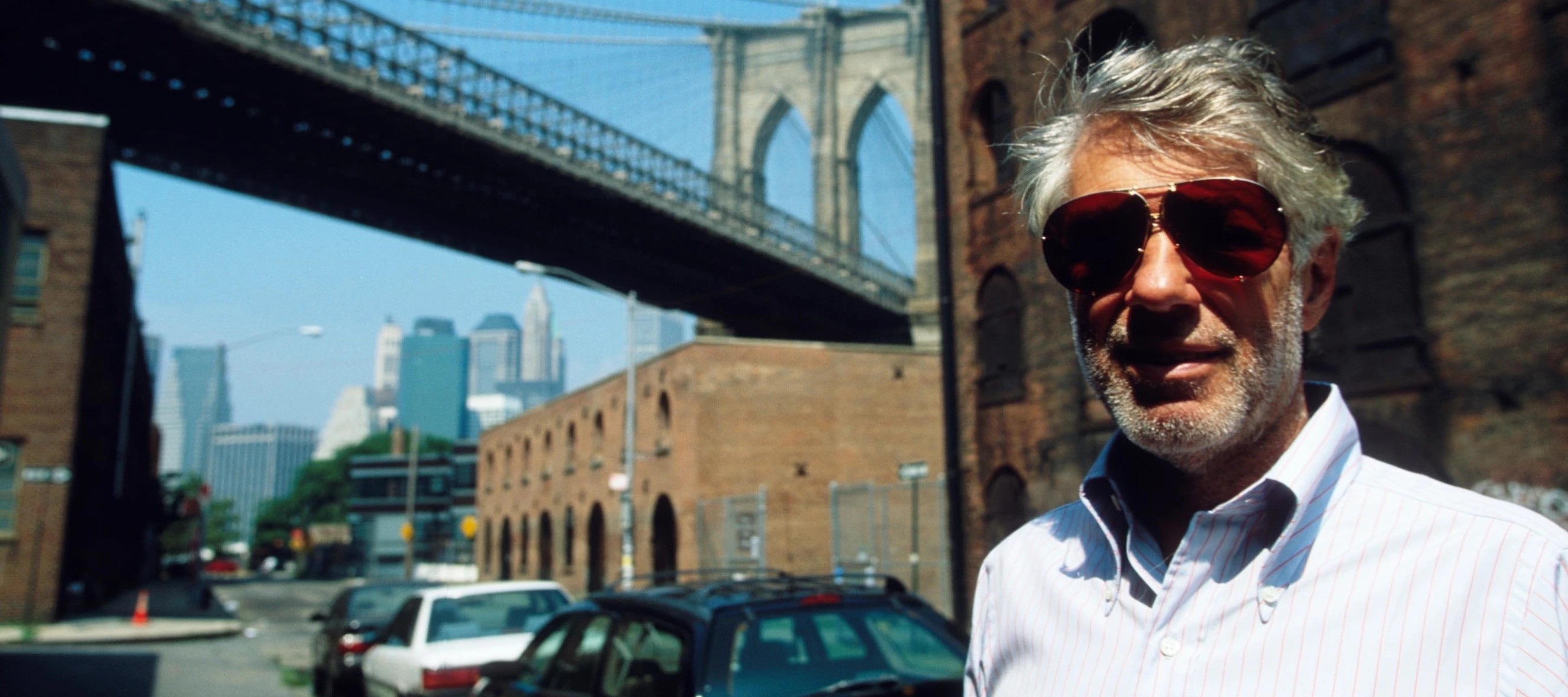 Man wearing sunglasses standing in front of a bridge