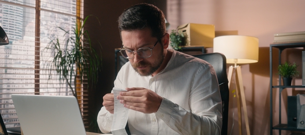 Man wearing glasses holding receipt sitting at a desk