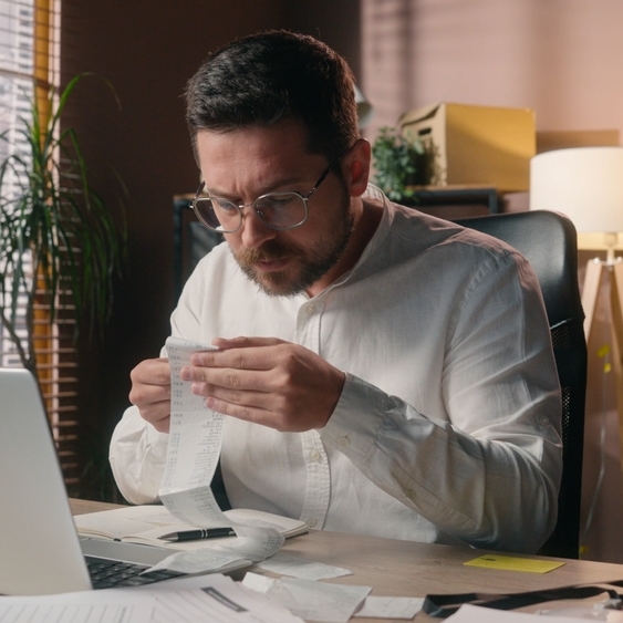 Man wearing glasses holding receipt sitting at a desk