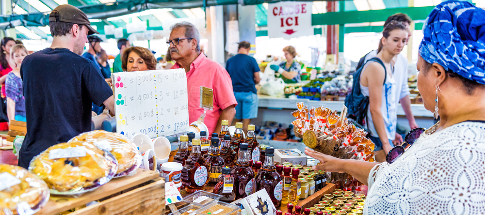 People walking by Maple Syrup products display store stand at Jean-Talon farmers market in Montreal, Quebec