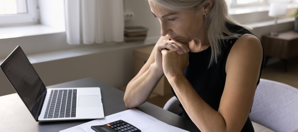Woman sitting at table with laptop, calculator and papers