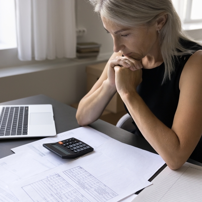 Woman sitting at table with laptop, calculator and papers