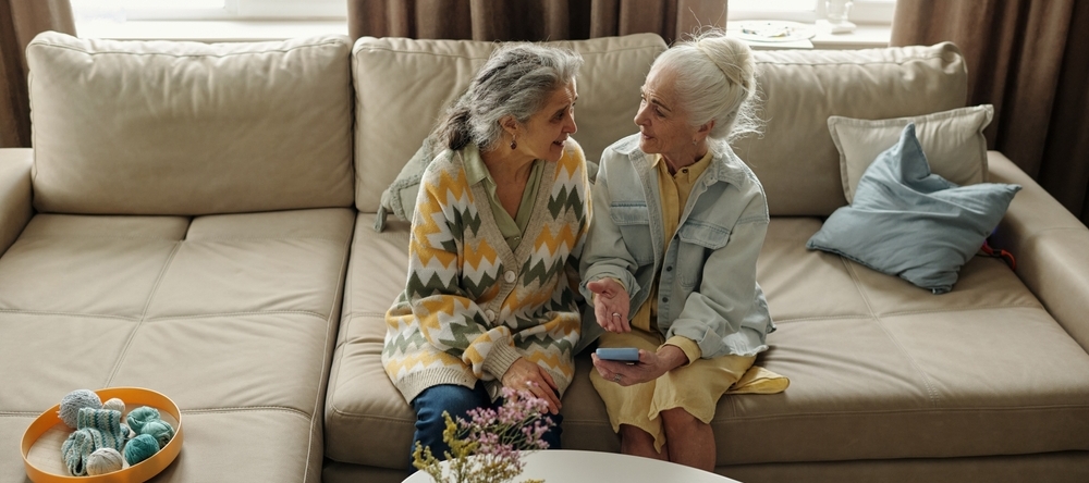 Two senior women sitting on a couch having a conversation