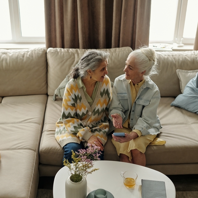 Two senior women sitting on a couch having a conversation