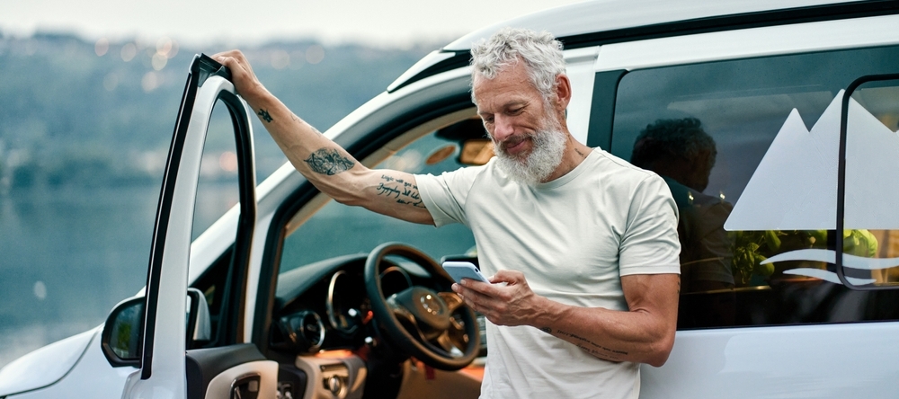 Tattooed elder man outside of car scrolling on his phone in the outdoors