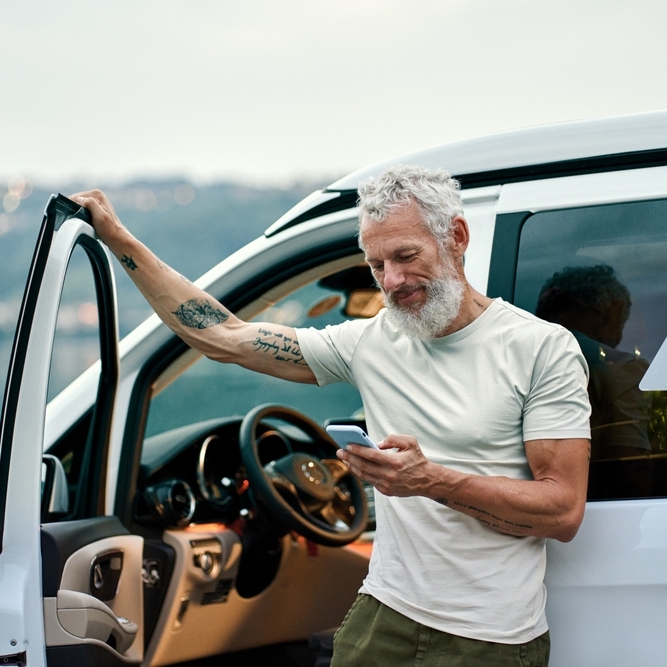 Tattooed elder man outside of car scrolling on his phone in the outdoors