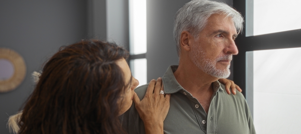 Middle-aged woman hugging pensive-looking middle-aged man