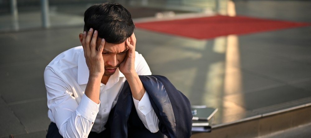 Man in suit, sitting on street curb looking stressed