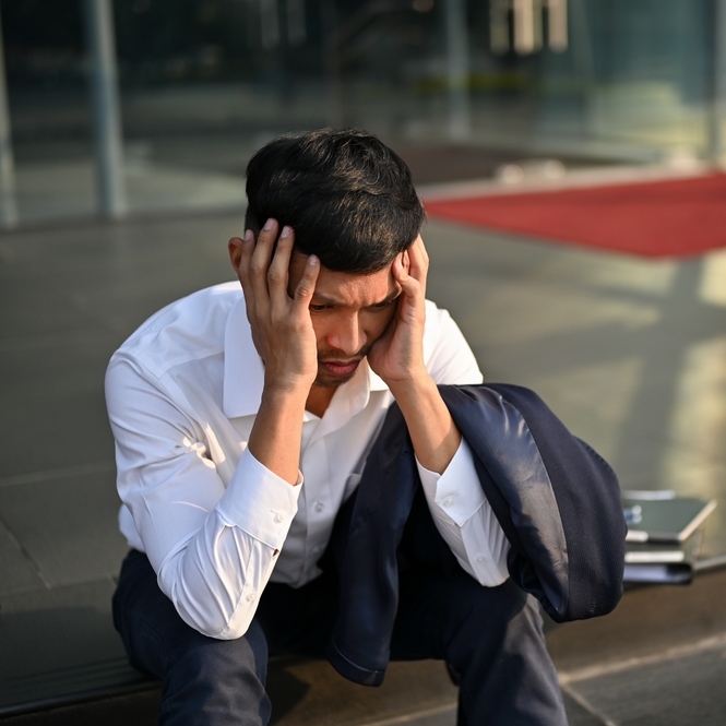 Man in suit, sitting on street curb looking stressed