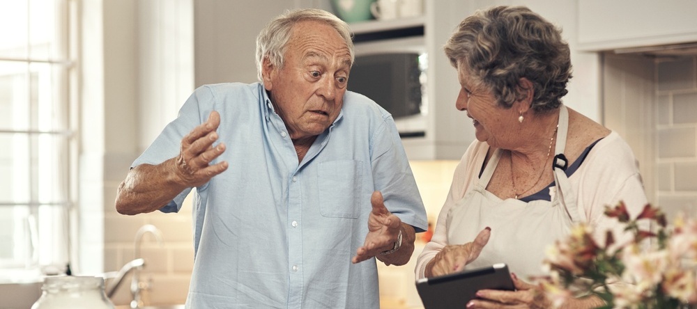 Older couple in the kitchen, talking, looking at tablet looking confused