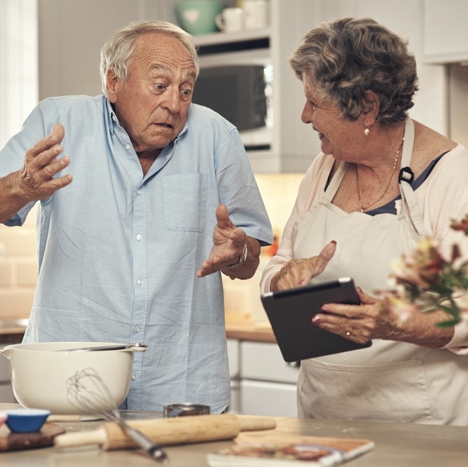 Older couple in the kitchen, talking, looking at tablet looking confused