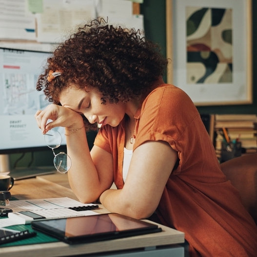 Woman sitting on desk, holding her glasses looking stressed