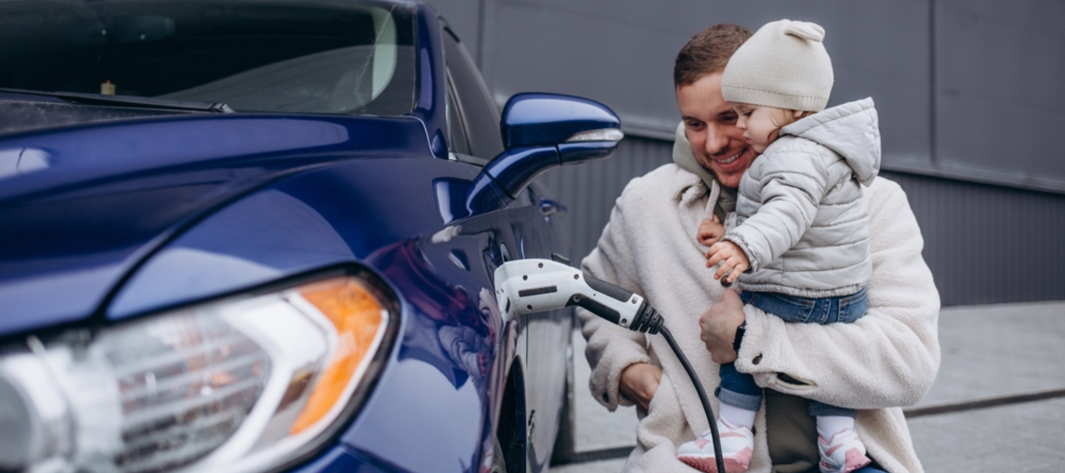 young father with daughter in his arms charging an electric car