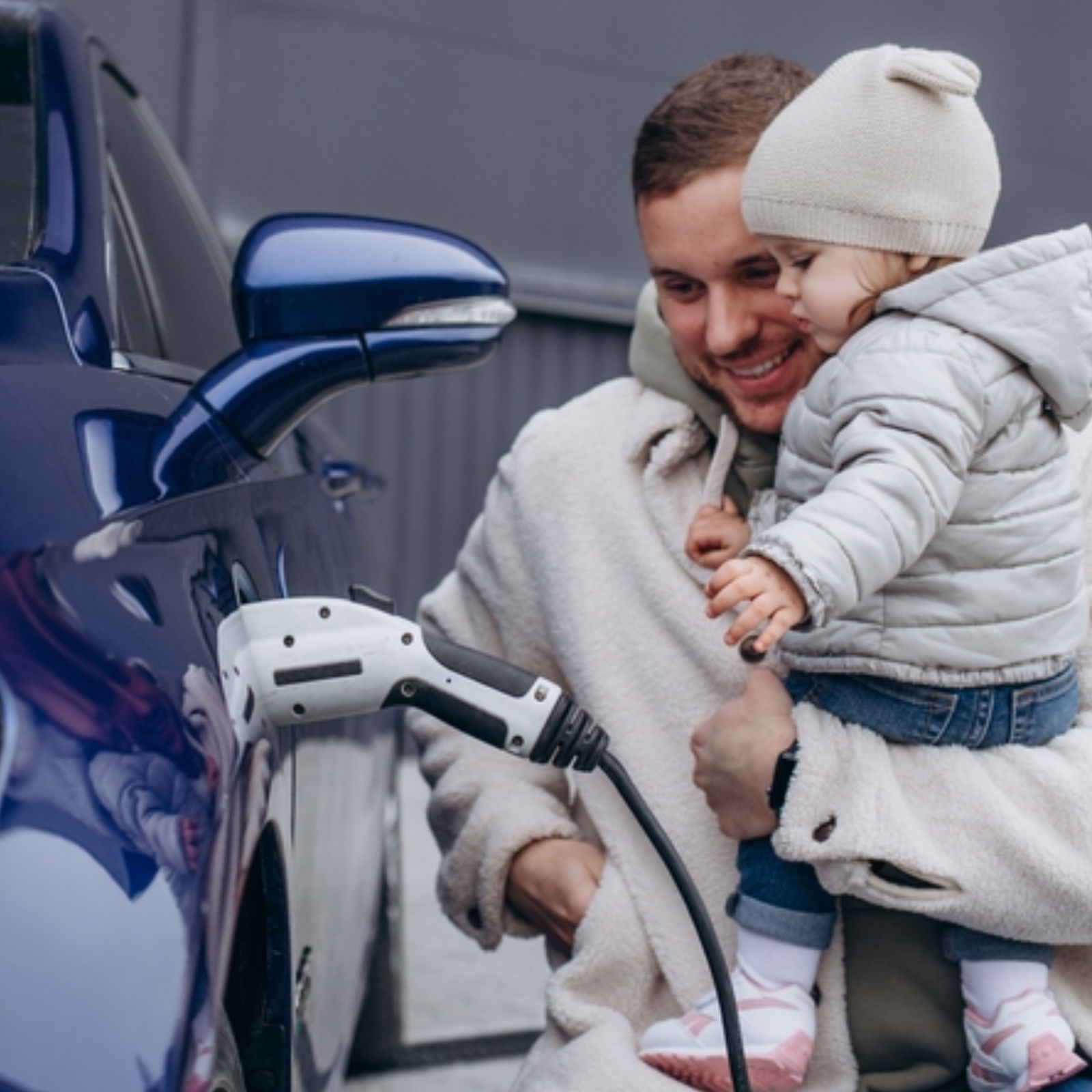 young father with daughter in his arms charging an electric car