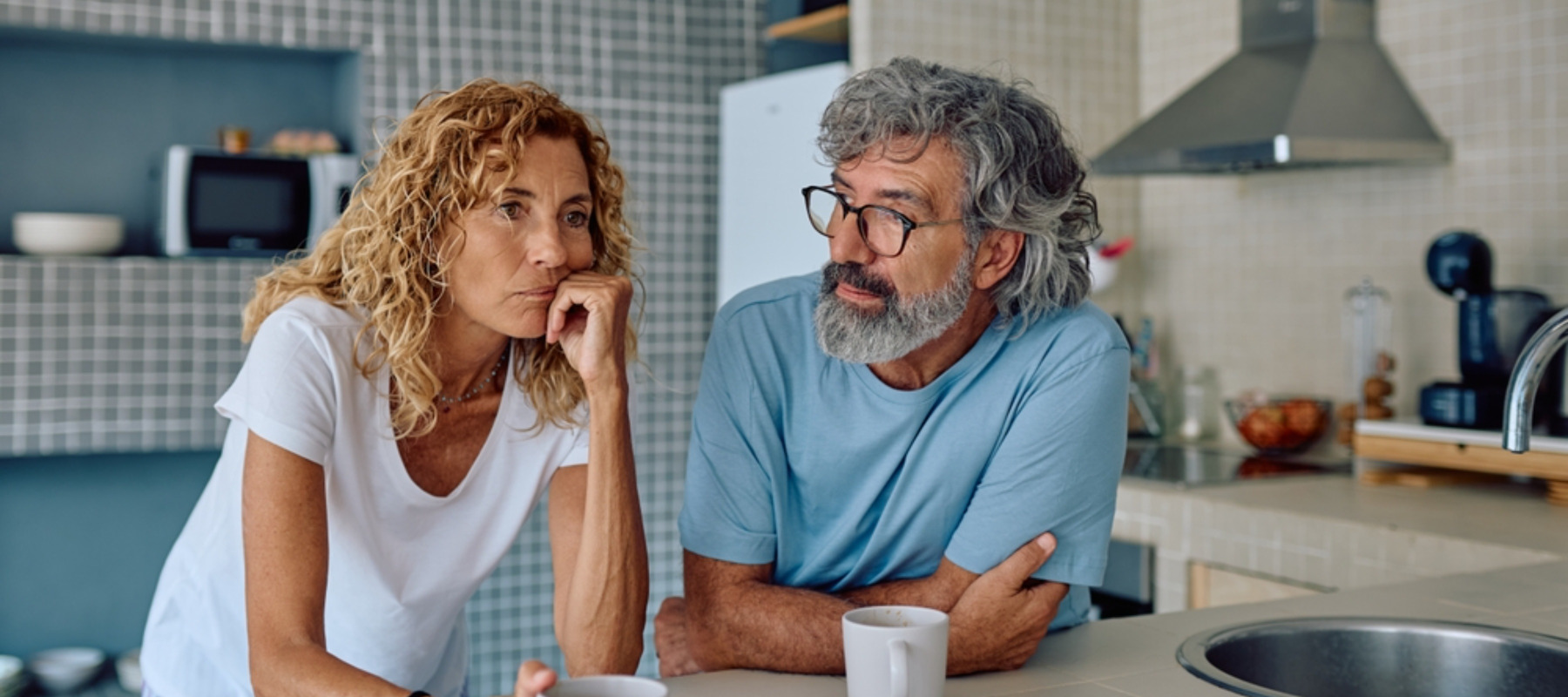 Senior couple sharing breakfast in their modern kitchen, discussing their worries and challenges while sipping coffee and tea together