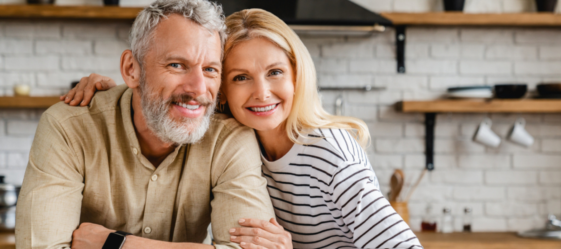 Portrait of middle aged couple hugging while standing together in kitchen at home
