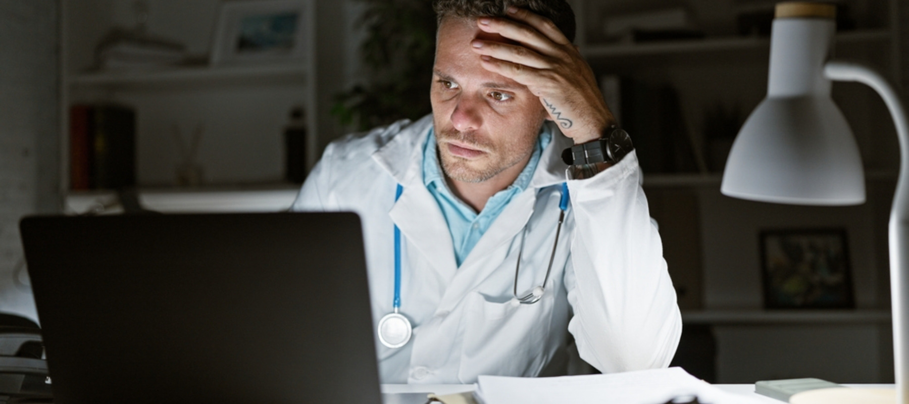 Tired doctor working late in the hospital office with laptop and paperwork