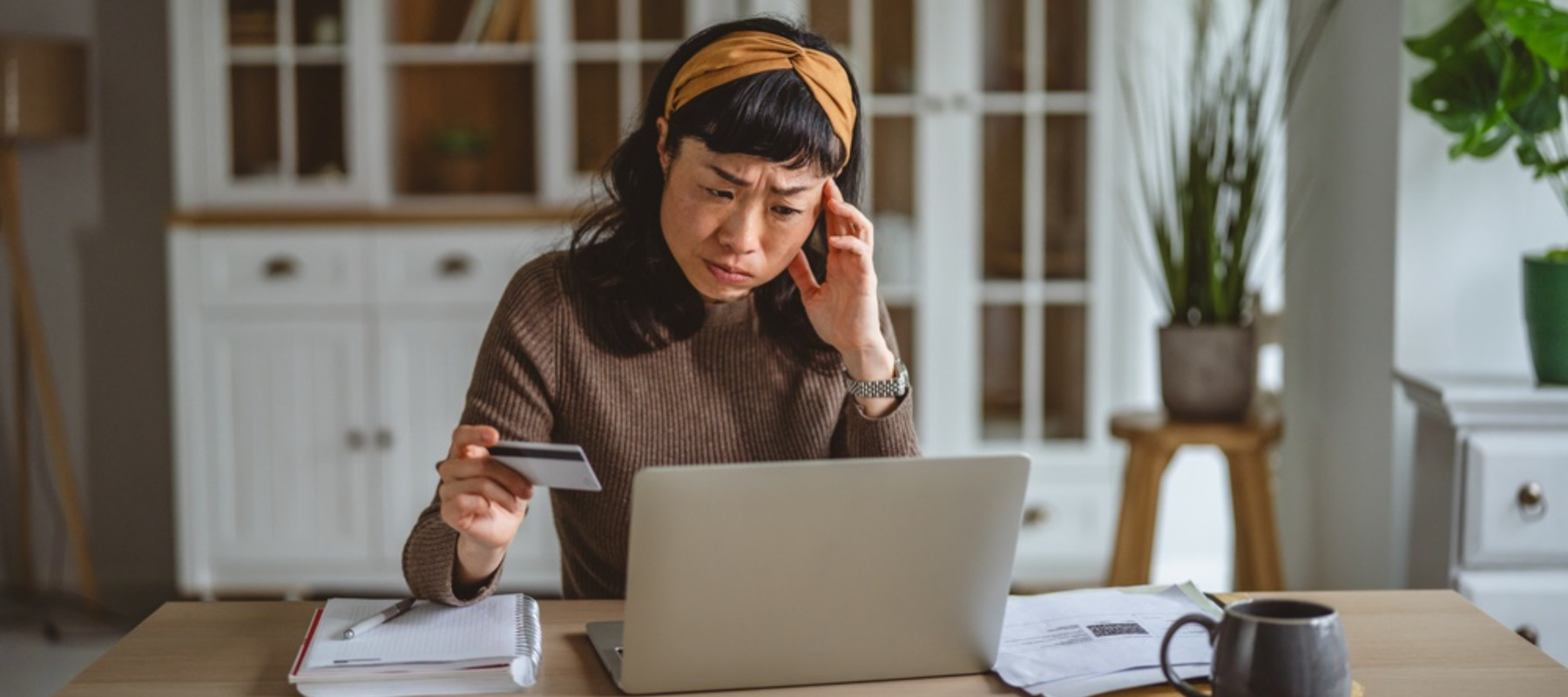 Woman feeling overwhelmed and stressed while trying to manage finances, looking intently at her laptop screen and holding a credit card to make payments at home