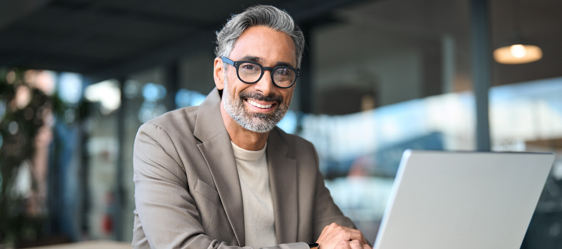Smiling middle aged businessman wearing glasses sitting at outdoor office table using laptop