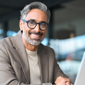 Smiling middle aged businessman wearing glasses sitting at outdoor office table using laptop