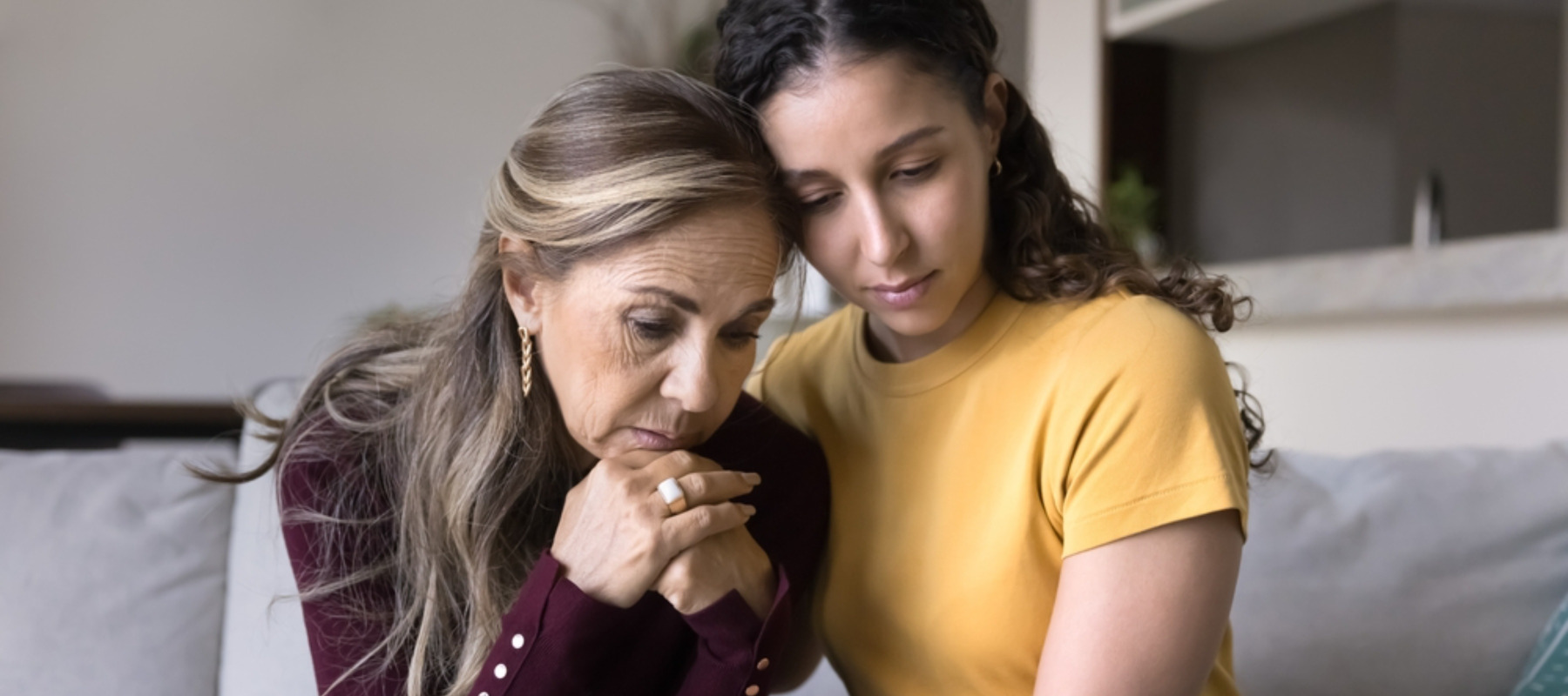 Sad young adult Latin daughter comforting depressed senior mom at home