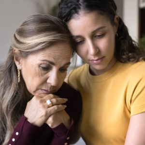 Sad young adult Latin daughter comforting depressed senior mom at home