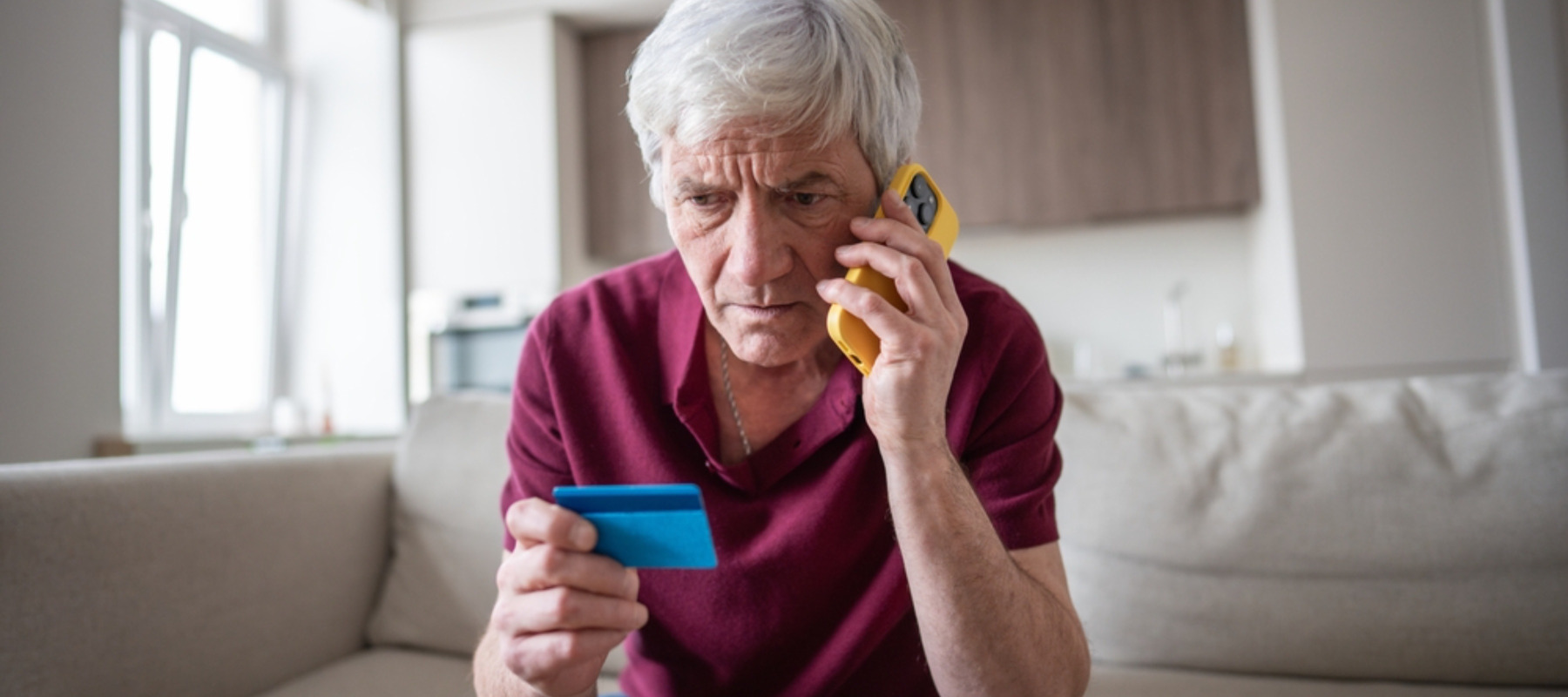 Senior man holding credit card looking worried and being scammed