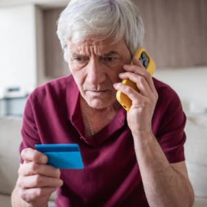 Senior man holding credit card looking worried and being scammed