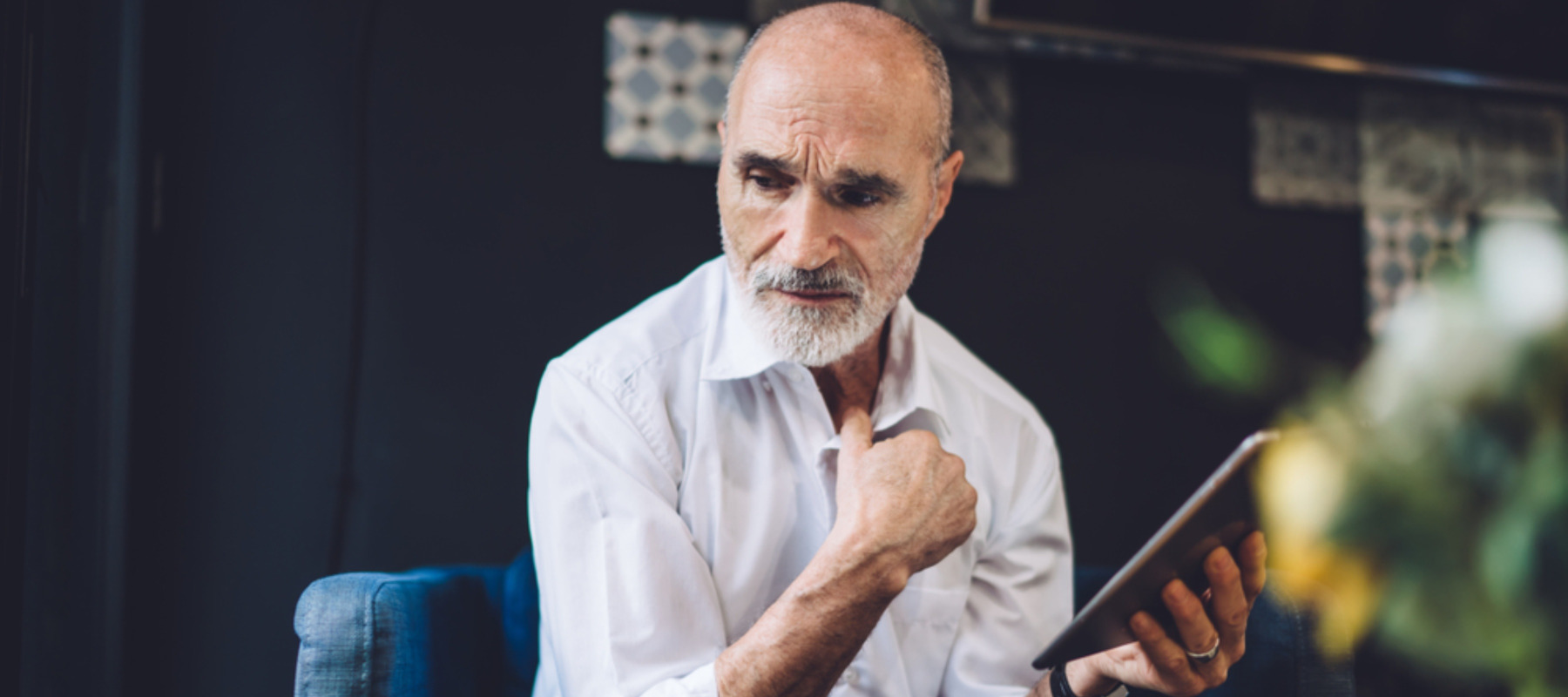 Confused gray haired bald 60 years old male in formal clothes browsing modern tablet with bewilderment