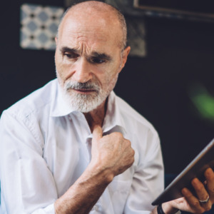 Confused gray haired bald 60 years old male in formal clothes browsing modern tablet with bewilderment